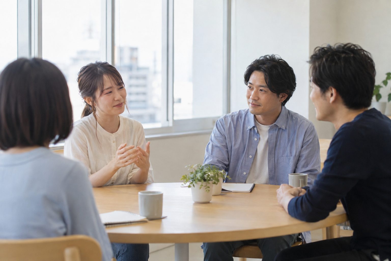 明るい部屋の丸いテーブルを囲み、穏やかな表情で話を聞き合う4人
